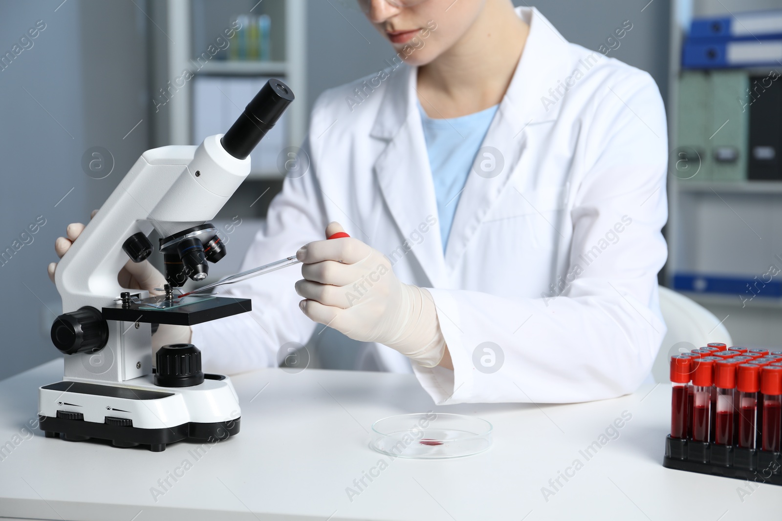 Photo of Laboratory testing. Doctor dripping blood sample onto glass slide while working with microscope at table indoors, closeup