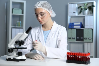 Laboratory testing. Doctor dripping blood sample onto glass slide while working with microscope at table indoors