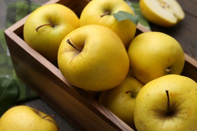 Ripe yellow apples in wooden crate on table, closeup