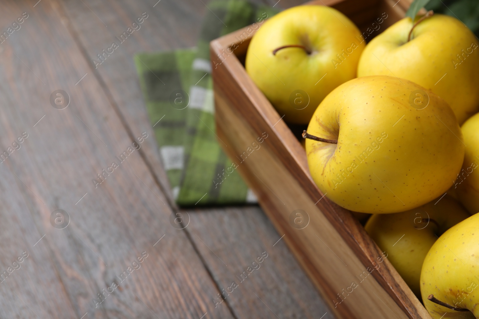 Photo of Ripe yellow apples in crate on wooden table, closeup. Space for text