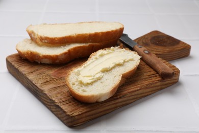 Photo of Fresh bread with butter and knife on white tiled table, closeup