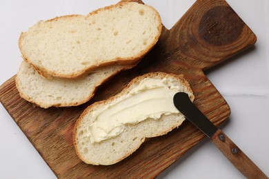 Photo of Fresh bread with butter and knife on white tiled table, top view