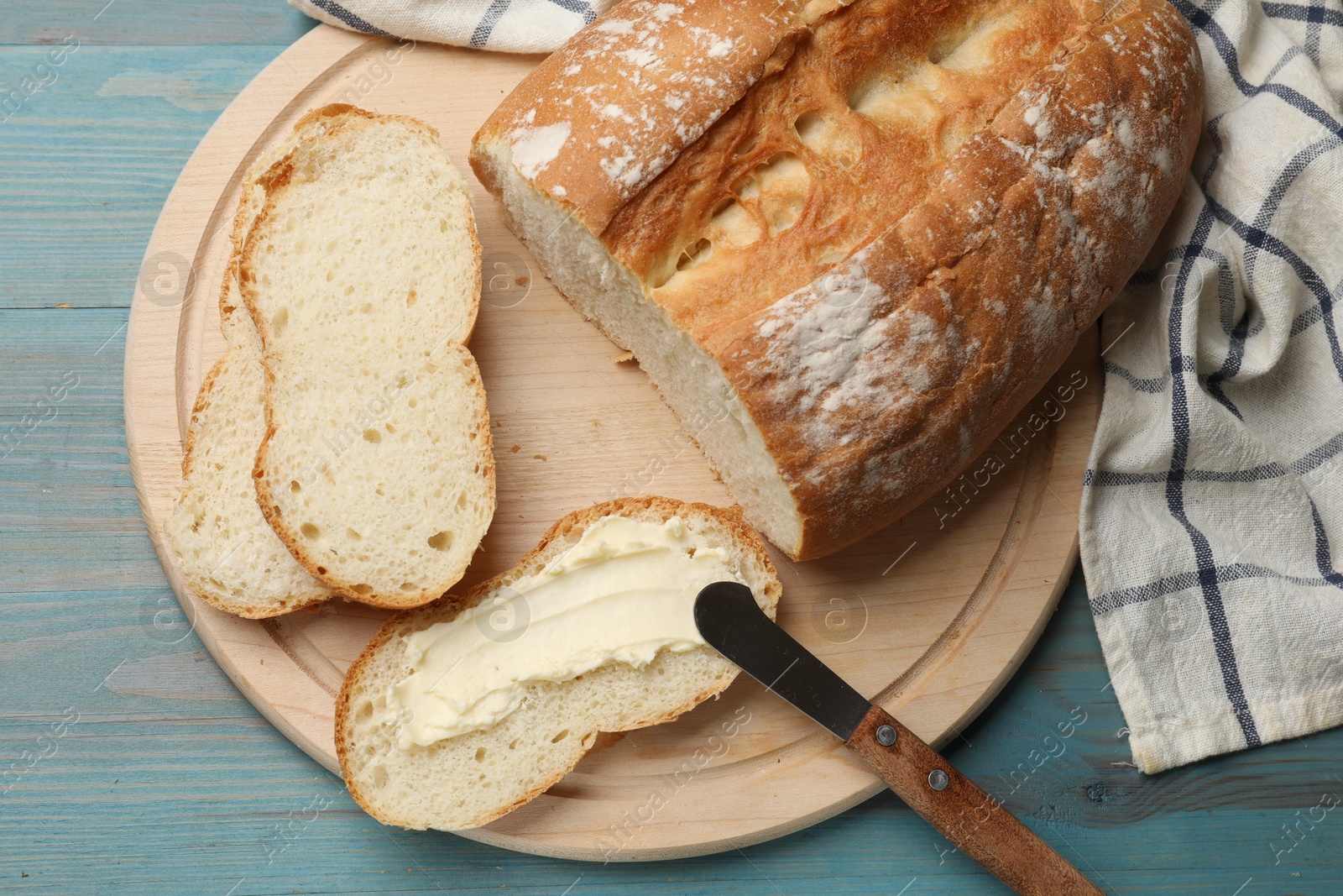 Photo of Fresh bread with butter and knife on blue wooden table, top view