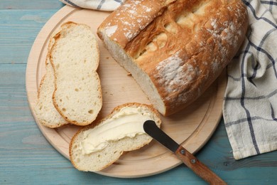 Photo of Fresh bread with butter and knife on blue wooden table, top view