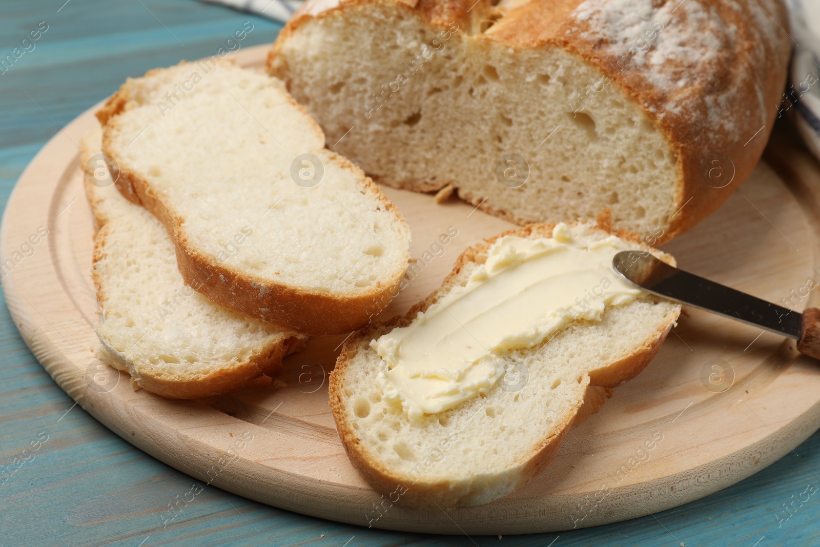 Photo of Fresh bread with butter and knife on blue wooden table, closeup