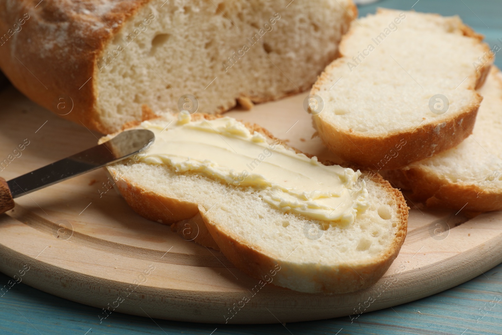 Photo of Fresh bread with butter and knife on blue wooden table, closeup