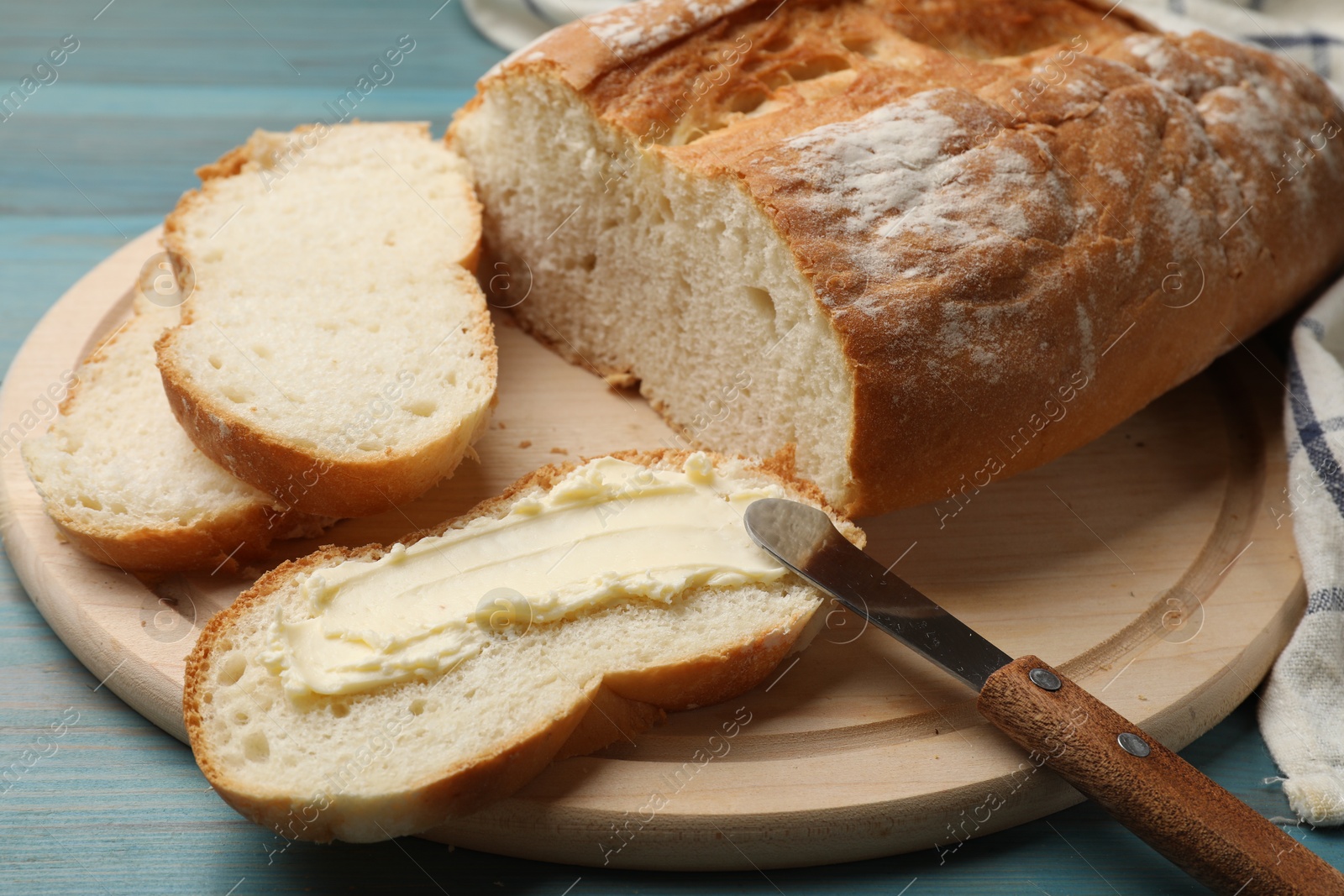 Photo of Fresh bread with butter and knife on blue wooden table, closeup