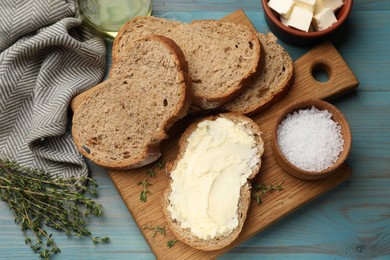 Photo of Fresh bread with butter, salt and thyme on blue wooden table, flat lay