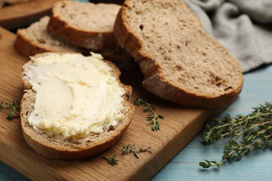 Photo of Fresh bread with butter and thyme on blue wooden table, closeup