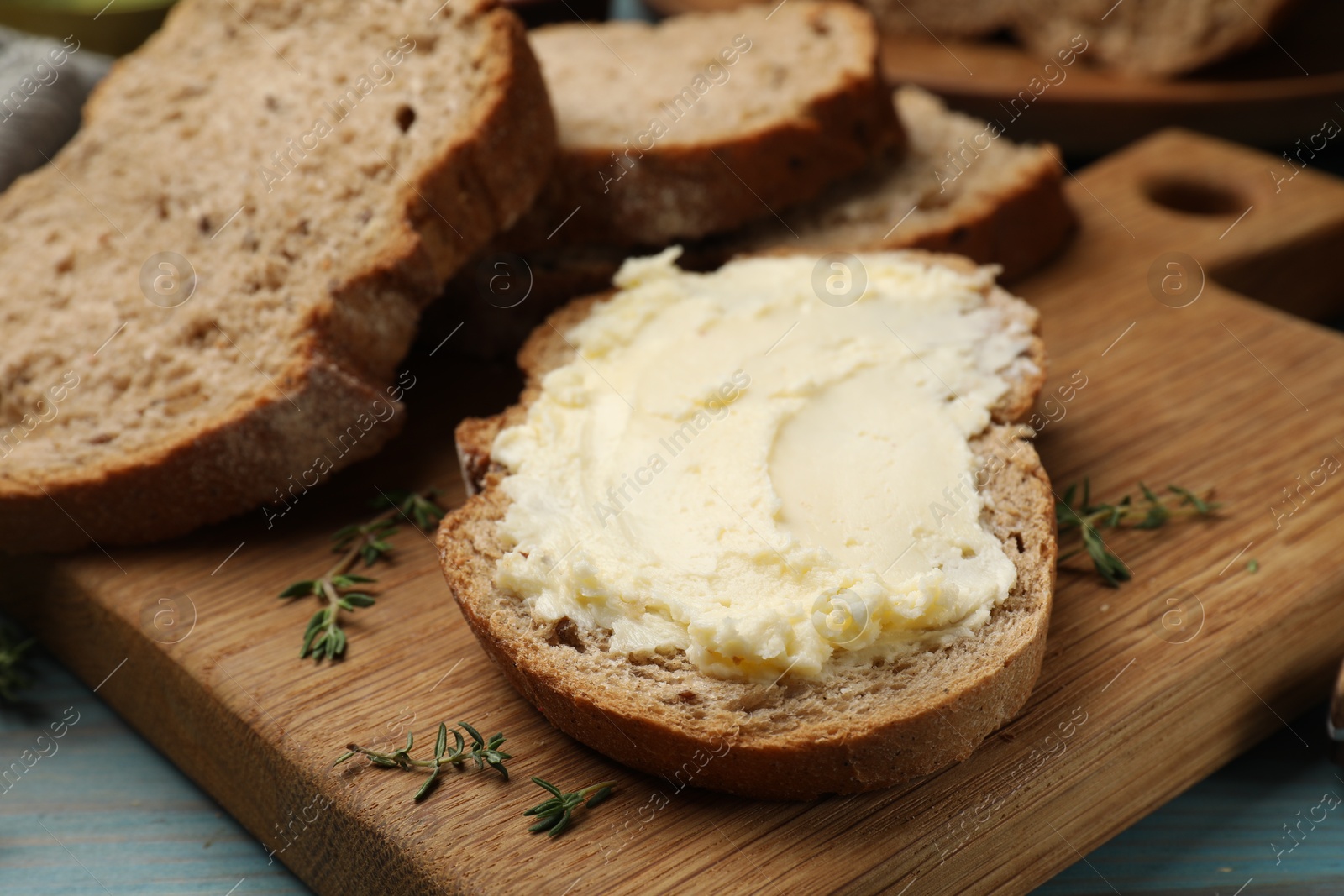 Photo of Fresh bread with butter and thyme on blue wooden table, closeup