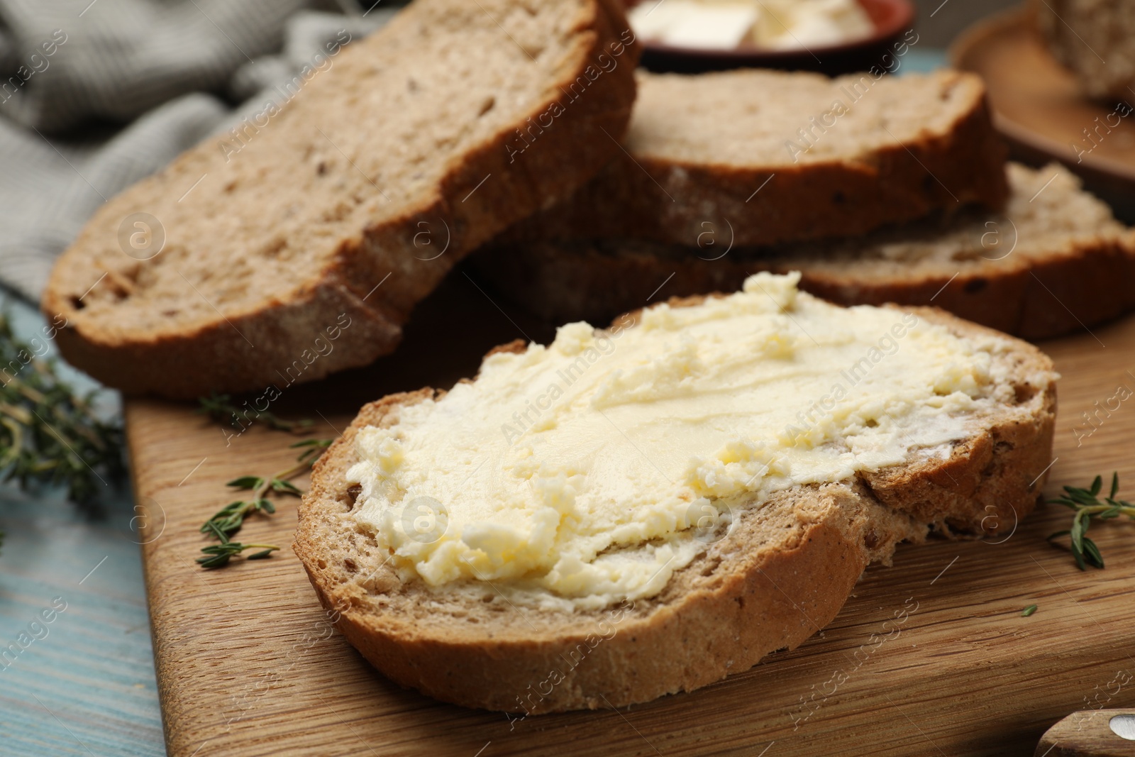 Photo of Fresh bread with butter and thyme on blue wooden table, closeup