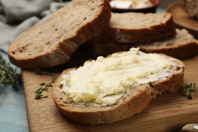 Photo of Fresh bread with butter and thyme on blue wooden table, closeup