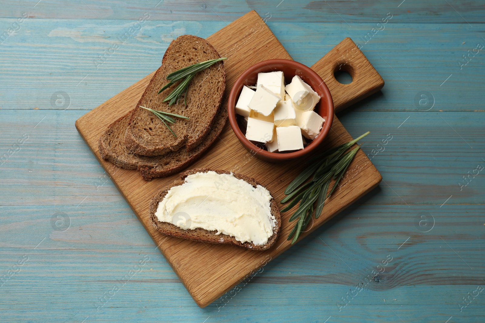 Photo of Fresh bread with butter and rosemary on blue wooden table, top view