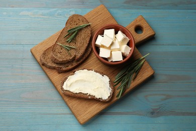 Photo of Fresh bread with butter and rosemary on blue wooden table, top view