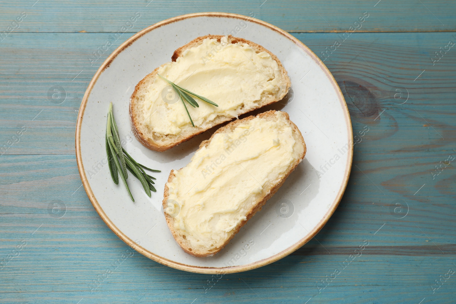 Photo of Fresh bread with butter and rosemary on blue wooden table, top view