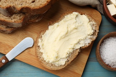 Photo of Fresh bread with butter, salt and knife on blue wooden table, flat lay