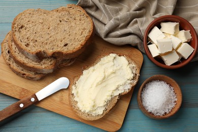 Photo of Fresh bread with butter, salt and knife on blue wooden table, flat lay