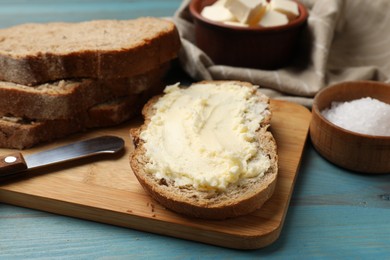 Photo of Fresh bread with butter, salt and knife on blue wooden table, closeup