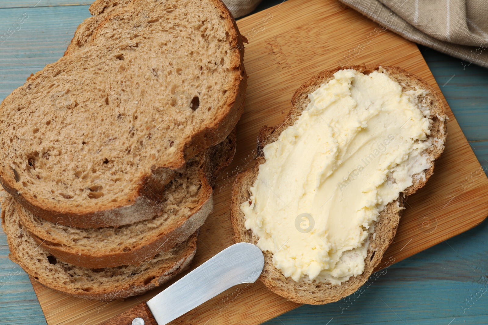 Photo of Fresh bread with butter and knife on blue wooden table, top view