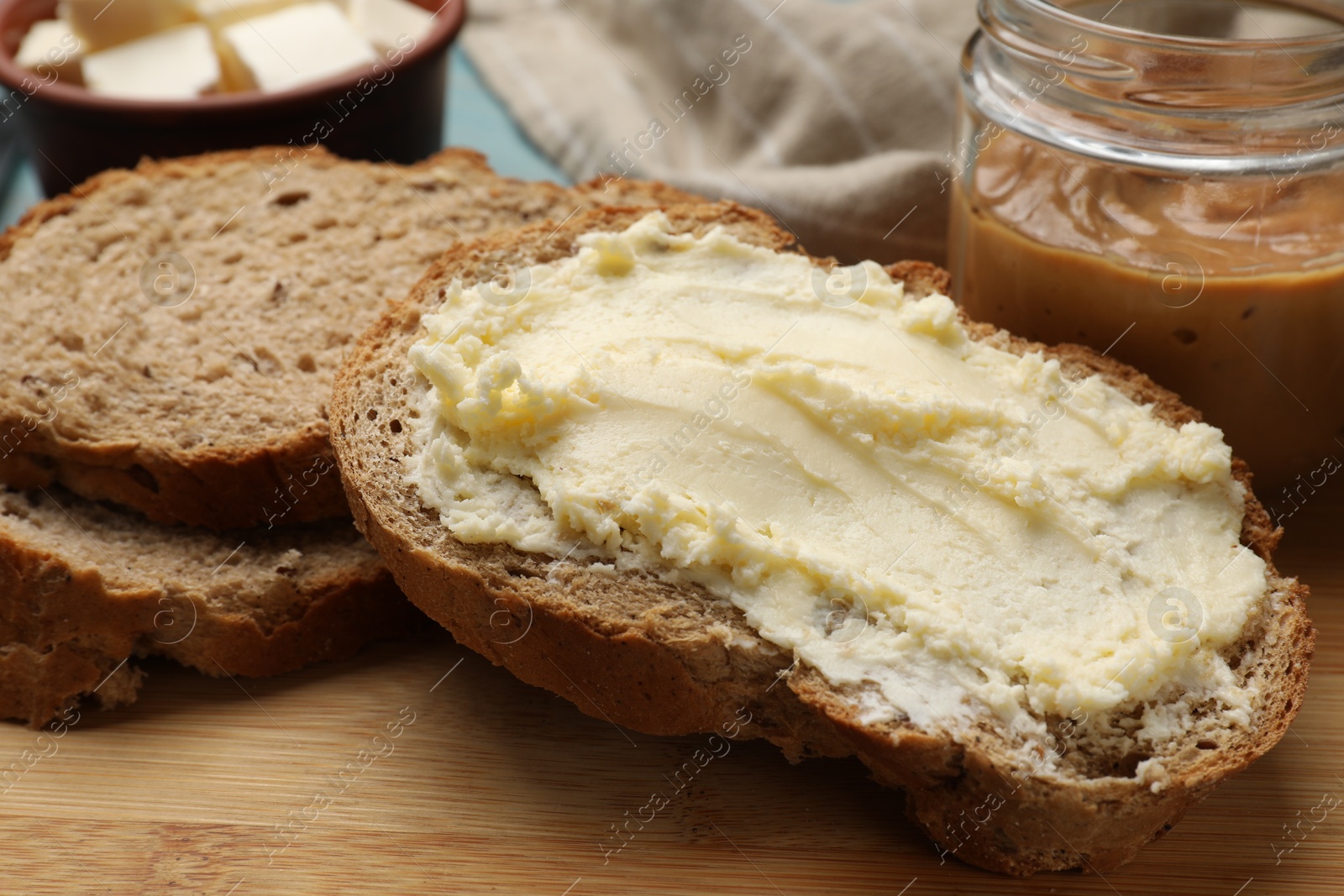 Photo of Fresh bread with butter and peanut paste on wooden table, closeup