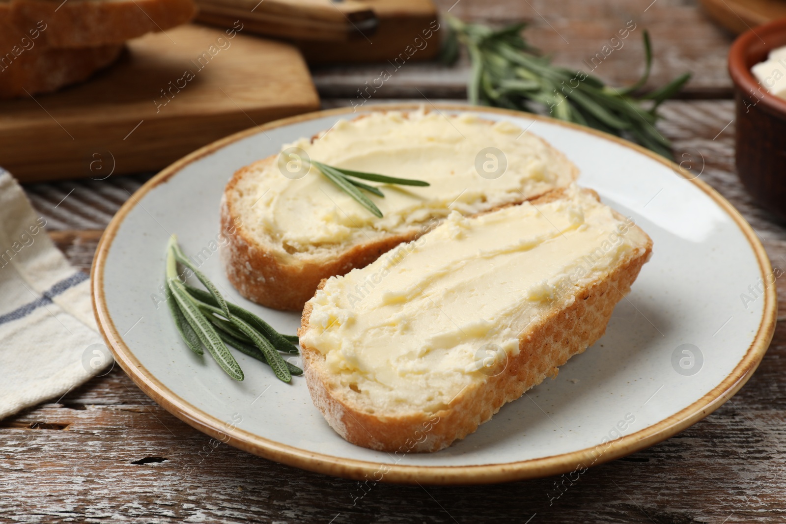 Photo of Fresh bread with butter and rosemary on wooden table, closeup