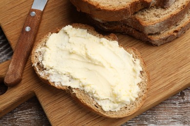 Photo of Fresh bread with butter and knife on wooden table, above view