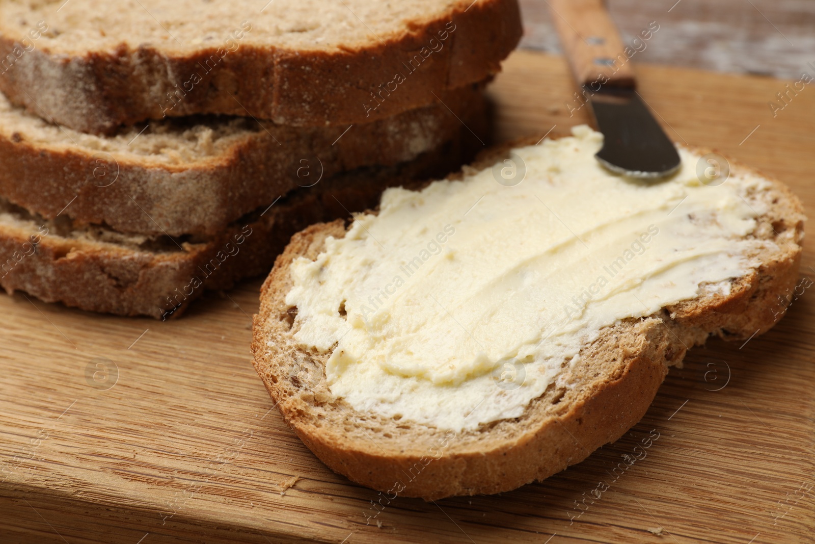 Photo of Fresh bread with butter and knife on wooden board, closeup