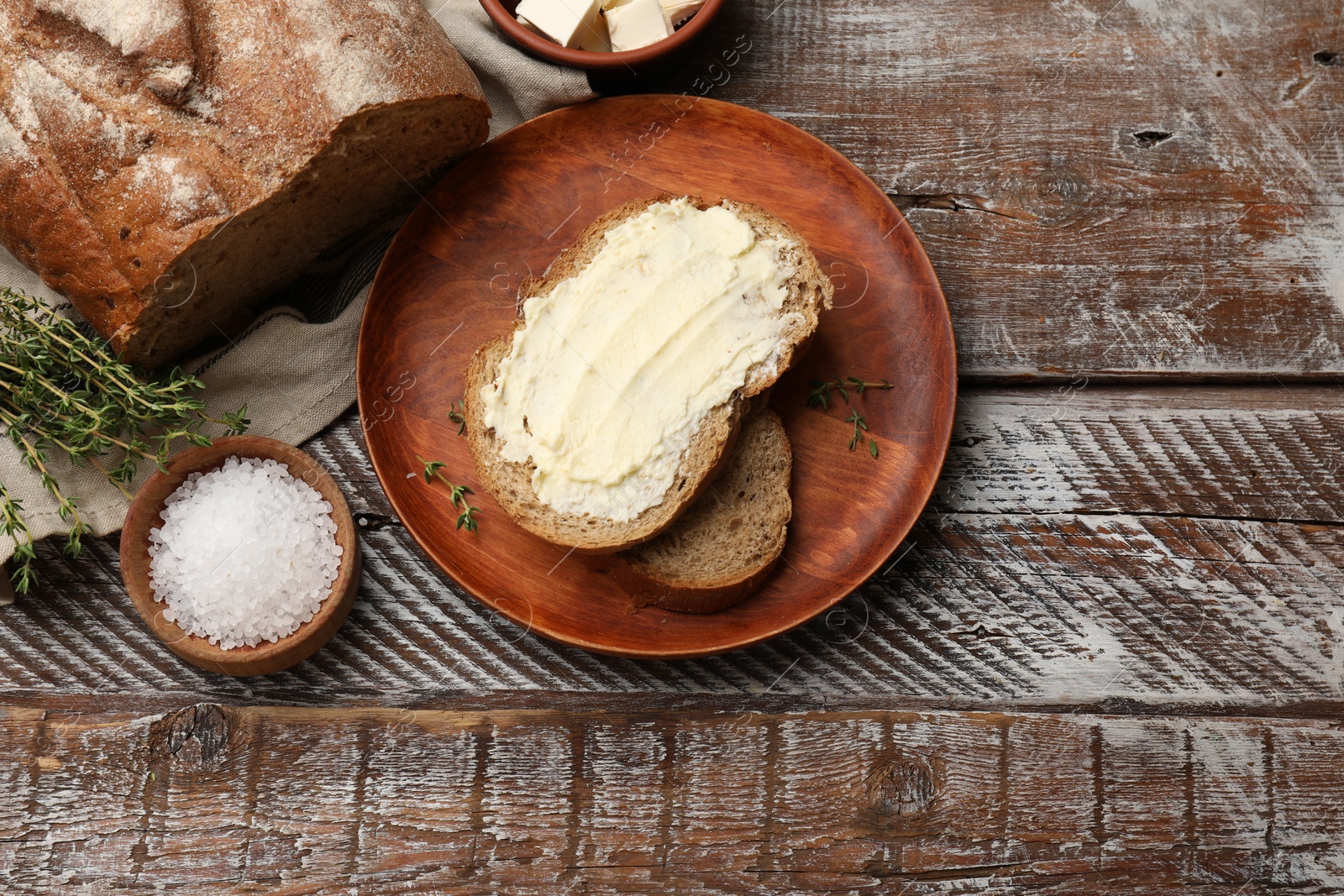 Photo of Fresh bread with butter, thyme and salt on wooden table, flat lay