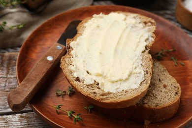 Photo of Fresh bread with butter and knife on wooden table, closeup