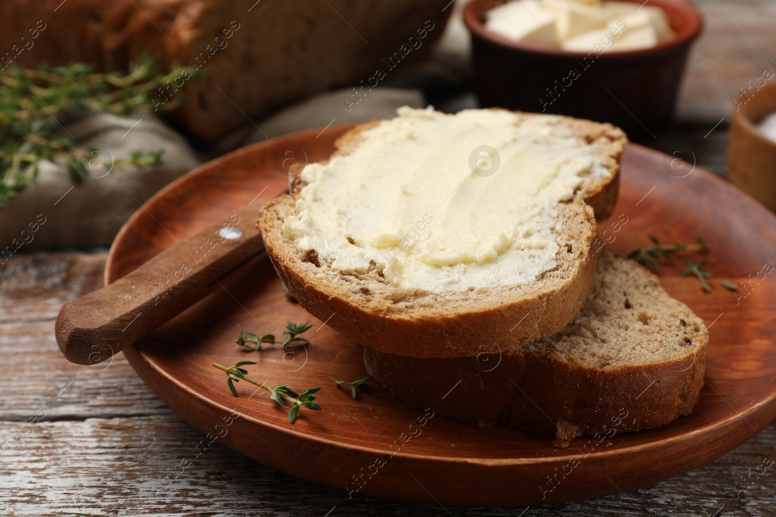 Photo of Fresh bread with butter and knife on wooden table, closeup