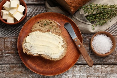 Photo of Fresh bread with butter, thyme, salt and knife on wooden table, flat lay