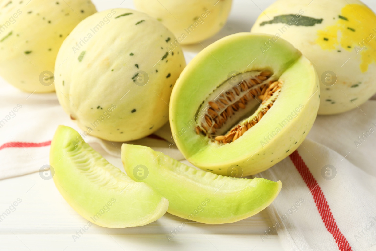 Photo of Fresh whole and cut honeydew melons on white wooden table, closeup