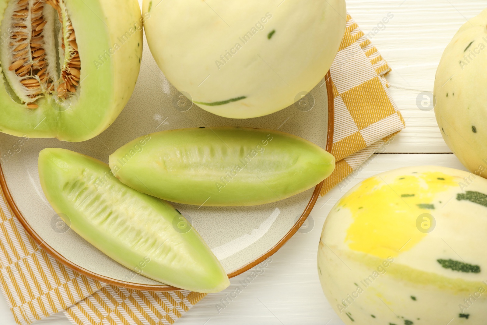 Photo of Fresh whole and cut honeydew melons on white wooden table, flat lay