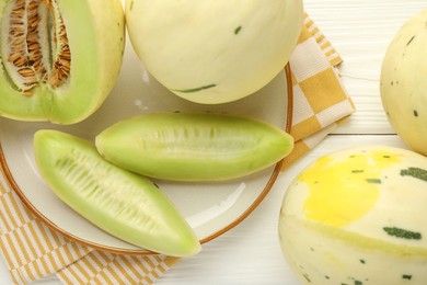 Photo of Fresh whole and cut honeydew melons on white wooden table, flat lay