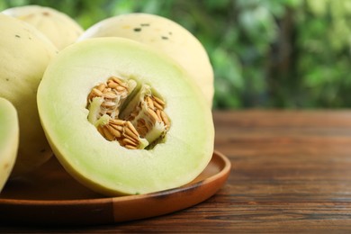 Photo of Fresh whole and cut honeydew melons on wooden table against blurred green background, closeup. Space for text