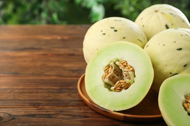 Photo of Fresh whole and cut honeydew melons on wooden table against blurred green background, closeup. Space for text