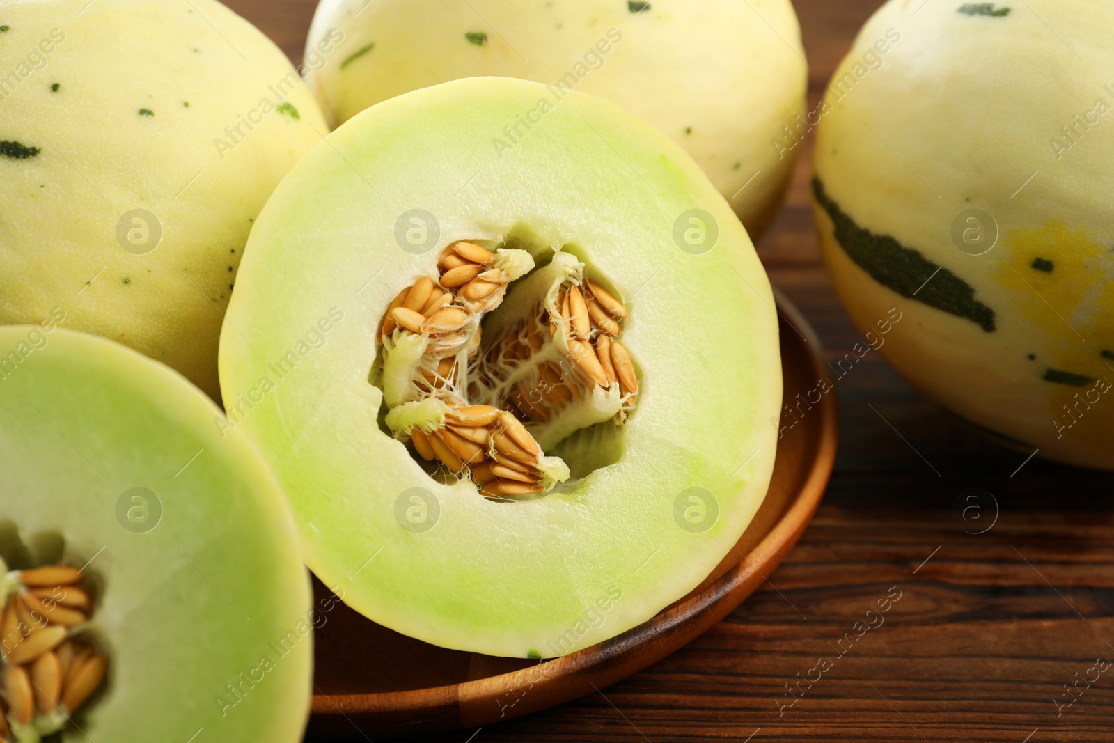 Photo of Fresh whole and cut honeydew melons on wooden table, closeup