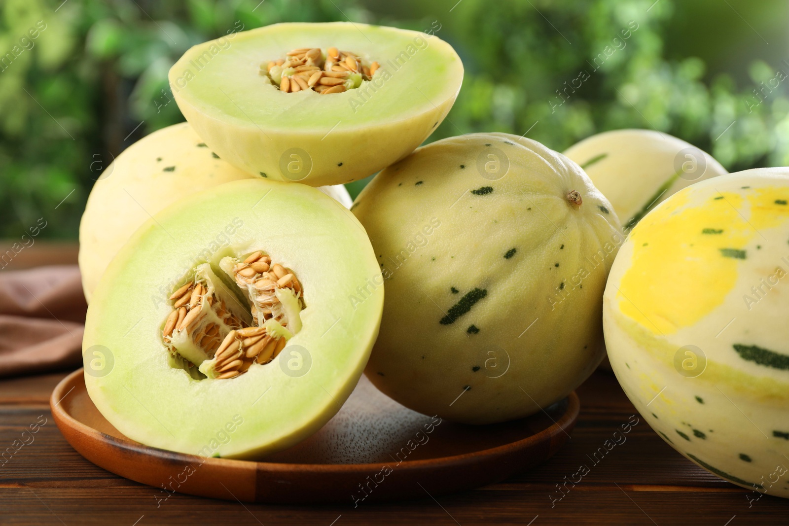 Photo of Fresh whole and cut honeydew melons on wooden table against blurred green background, closeup