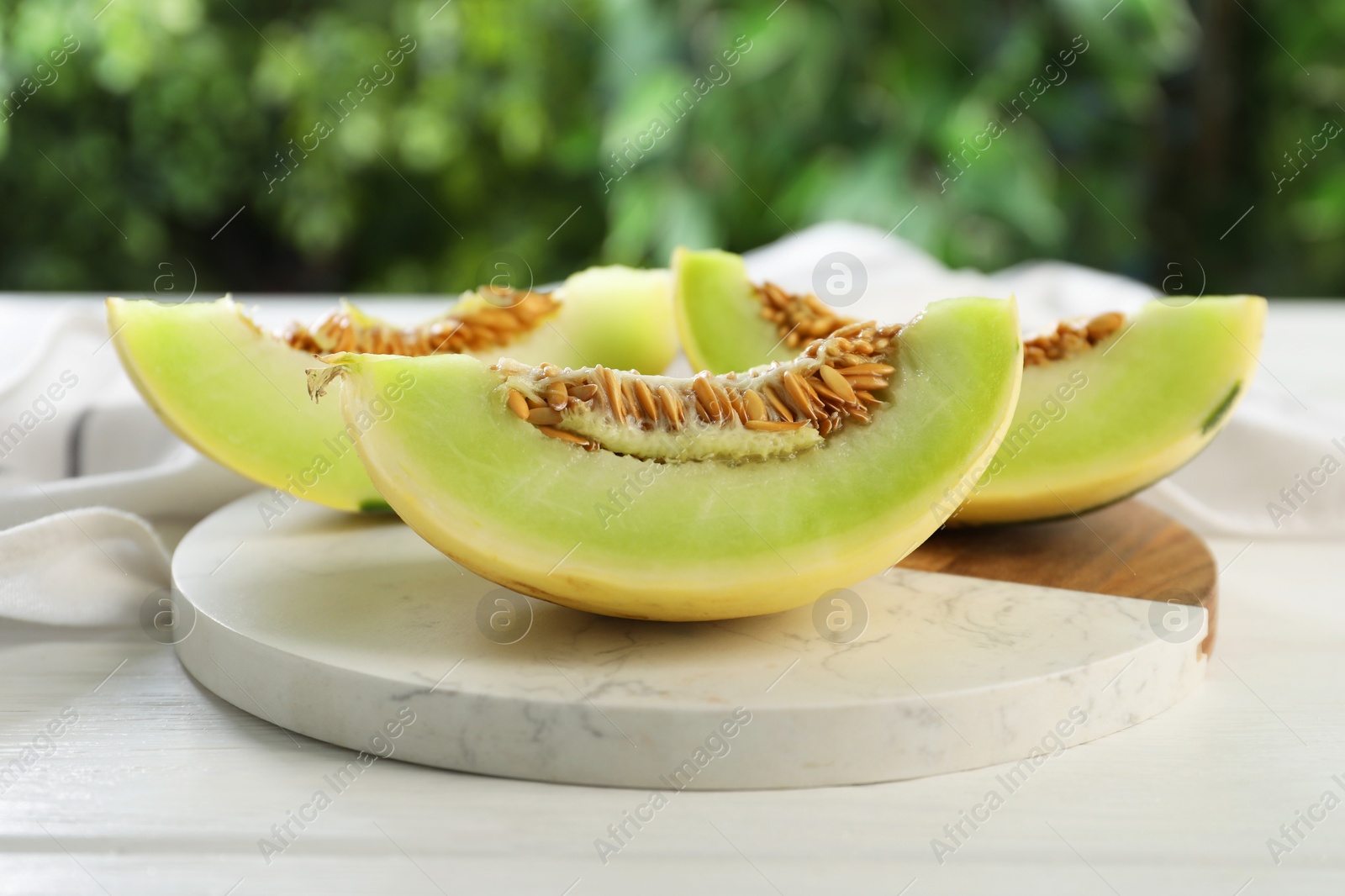 Photo of Fresh cut honeydew melon on white wooden table against blurred green background, closeup