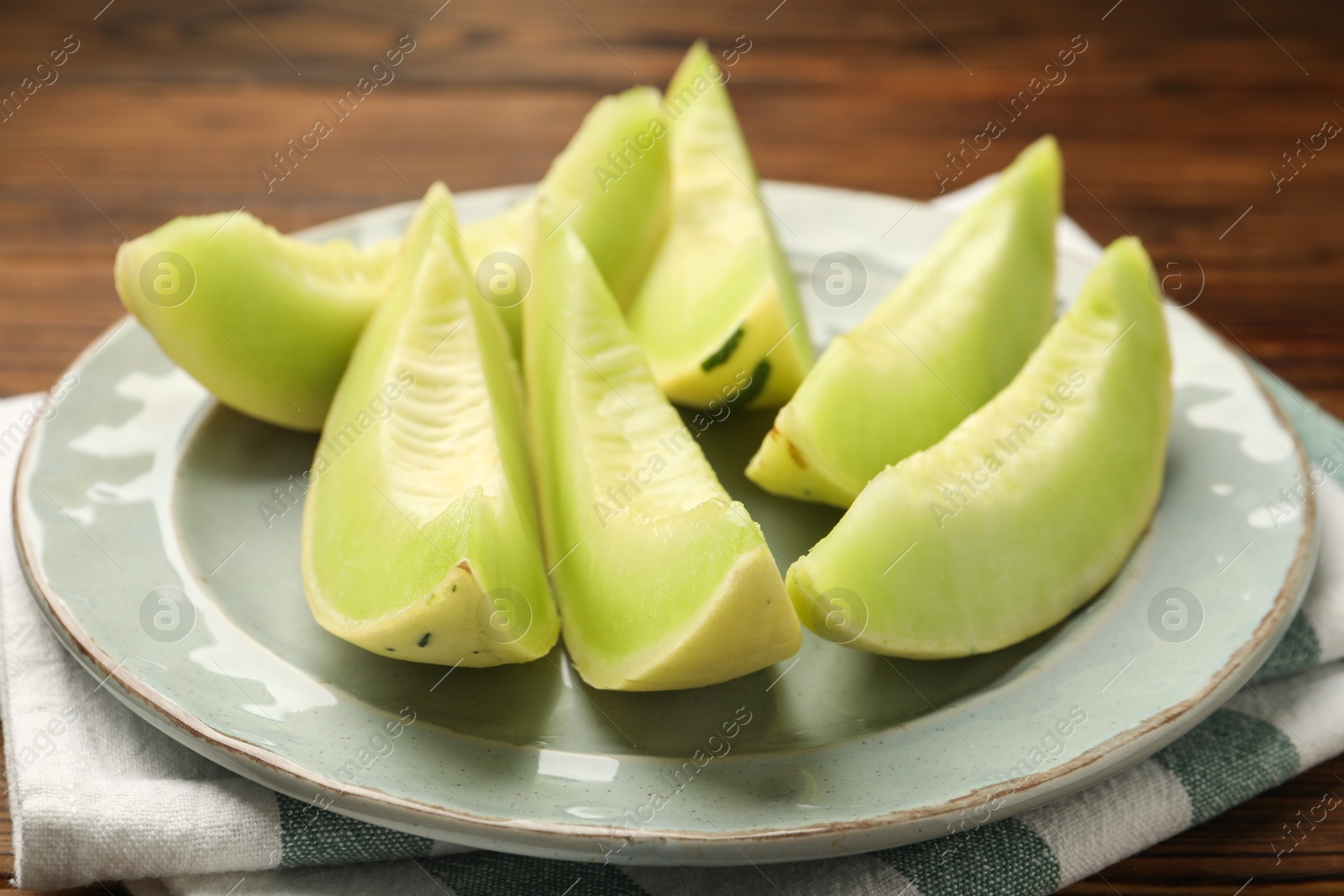 Photo of Plate with pieces of honeydew melon on wooden table, closeup