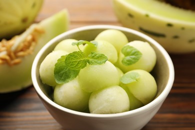 Photo of Melon balls in bowl and fresh fruit on wooden table, closeup