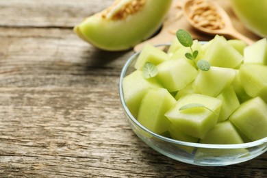 Photo of Slices of yummy melon in glass bowl on wooden table, closeup. Space for text