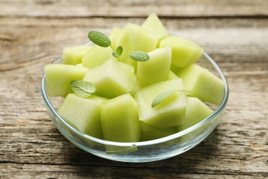 Photo of Slices of yummy melon in glass bowl on wooden table, closeup