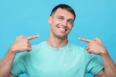 Smiling man pointing at his dental braces on light blue background