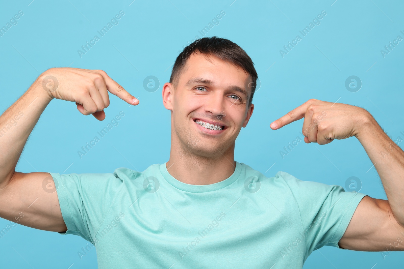 Photo of Smiling man pointing at his dental braces on light blue background