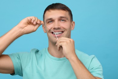 Man with braces cleaning teeth using dental floss on light blue background