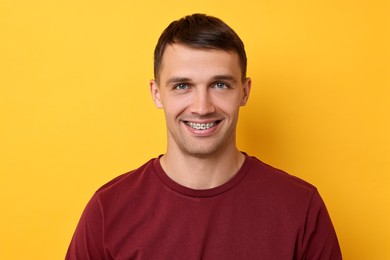 Smiling man with dental braces on yellow background