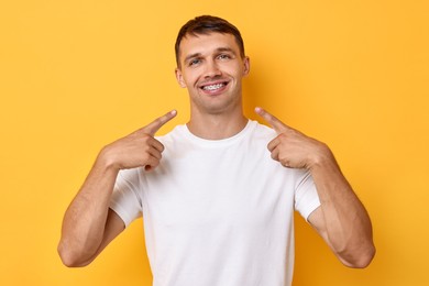 Smiling man pointing at his dental braces on yellow background