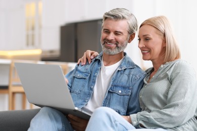 Happy middle aged couple using laptop on sofa indoors