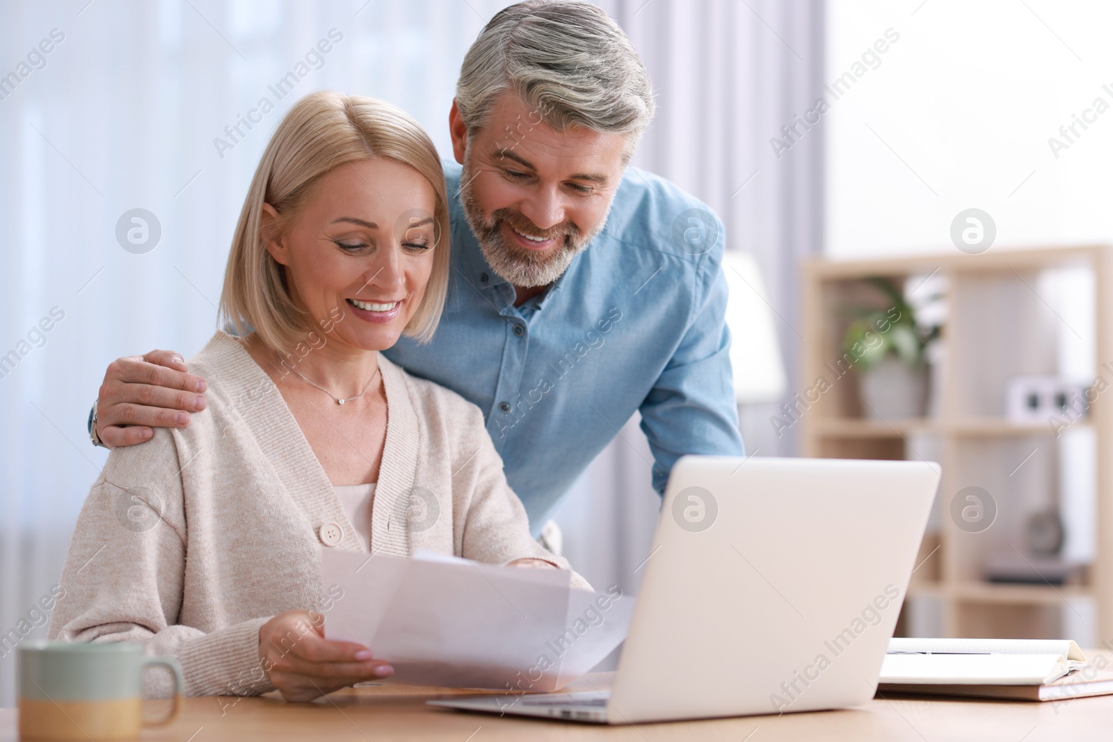 Photo of Happy middle aged couple working with laptop at table indoors